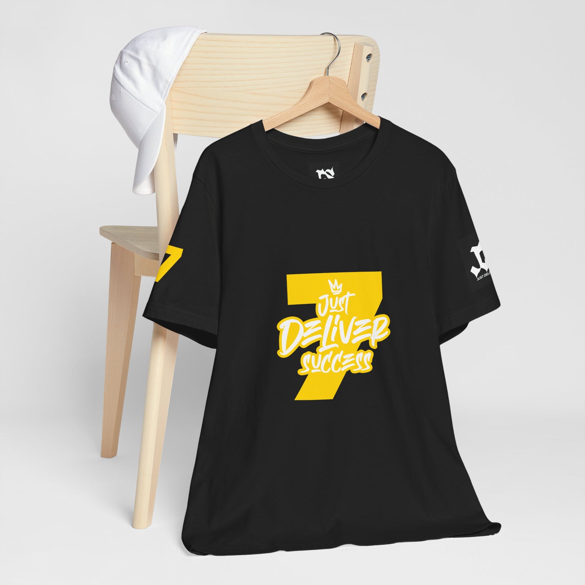 Just Deliver Success Gold That City 7 Summer Collection black t-shirt displayed on a wooden chair.
