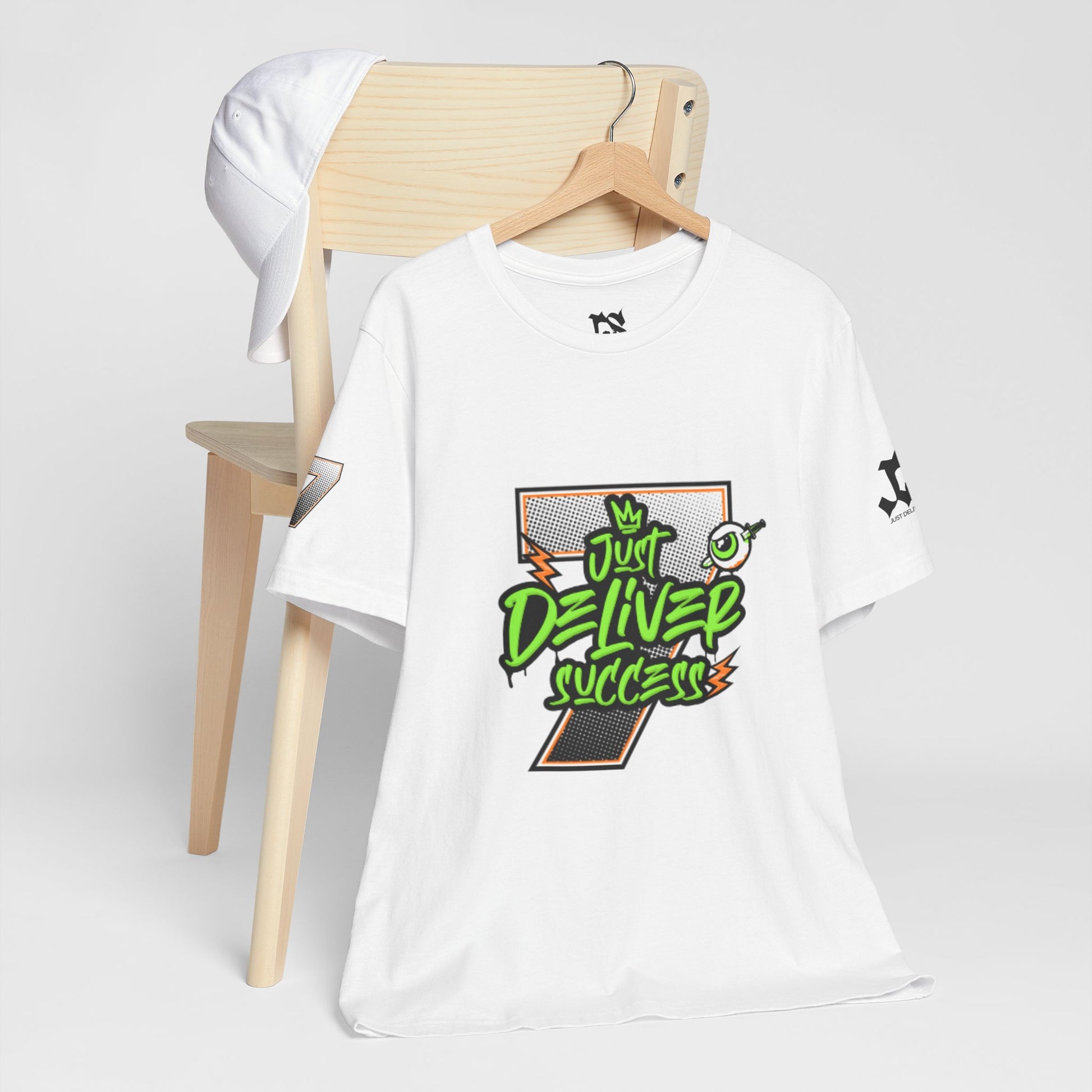 Just Deliver Success Da Desert That City 7 Summer Collection white t-shirt displayed on a wooden chair with a cap.