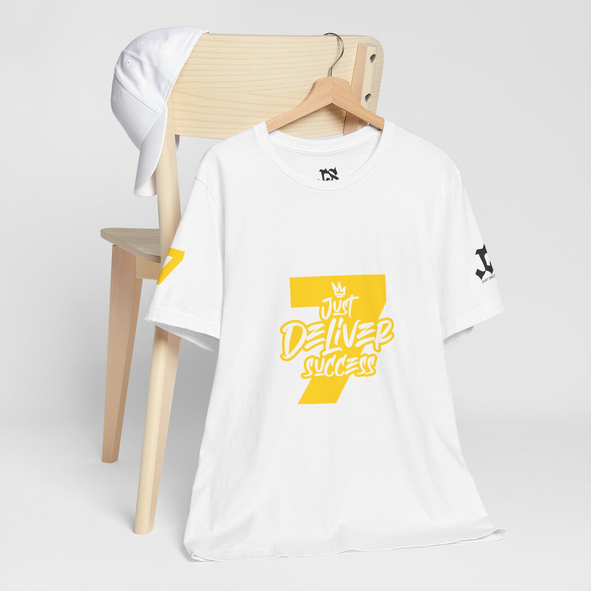 Just Deliver Success Gold That City 7 Summer Collection white t-shirt displayed on a chair with a cap.